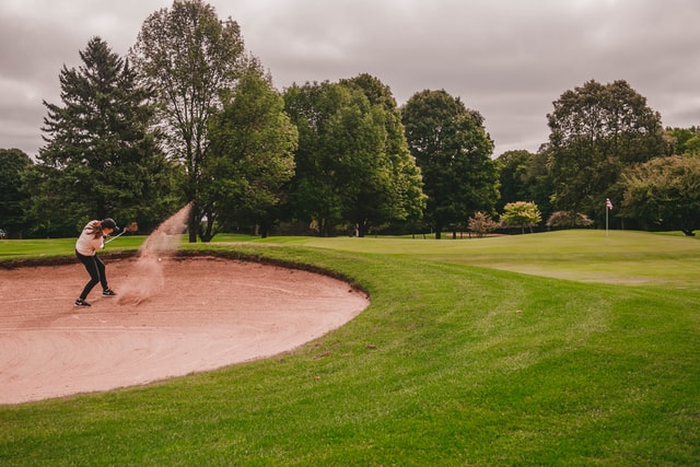 Woman hitting bunker shot with a sand wedge.